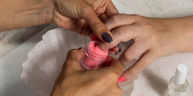 Manicurist using dip powder to give a girl a manicure