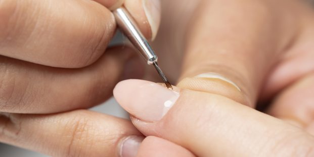 The manicurist is painting woman's fingernails with a thin brush in beauty salon.  Manicurist is using a brush in beauty salon. She is applying nail polish. Young woman getting a manicure. Beautiful hands and nails. Macro photo. Nail Care.